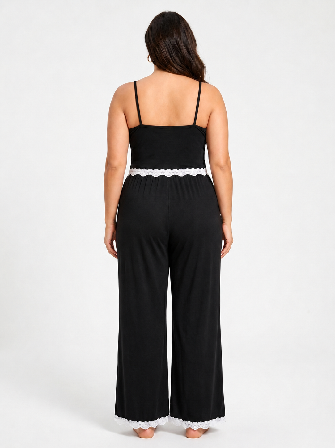 Back view of a woman in a black plus-size pajama jumpsuit with wide legs and white lace trim.