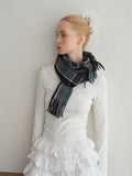 Woman with blonde hair pulled back, wearing a white long-sleeve top and ruffled skirt, with a dark plaid scarf draped around her shoulders.