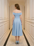 Rear view of a woman in a light blue off-the-shoulder midi dress with a fitted bodice and full skirt, standing in a hallway.