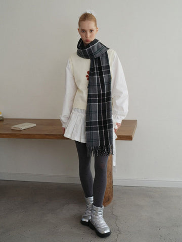 Woman wearing a white long-sleeve top, white pleated skirt, and grey polka dot tights, accessorized with a dark plaid scarf and silver boots.