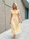Woman walking outdoors in a yellow floral print midi dress with ruffled neckline and short sleeves.