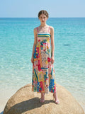 Woman in a maxi dress with a colorful print standing on a rock by the sea