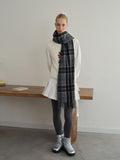 Full body shot of a woman in a white vest over a white long-sleeve shirt, a white pleated skirt, grey polka dot tights, and silver boots, with a dark plaid scarf.
