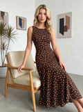 Woman sitting on a chair wearing a brown polka dot sleeveless midi dress