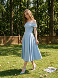 Woman in a light blue off-the-shoulder midi dress with a fitted bodice and full skirt, walking in a grassy outdoor setting.