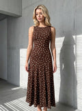 Woman in a brown polka dot sleeveless midi dress standing against a textured wall with blinds shadow