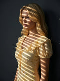 Close-up profile of a woman wearing a yellow floral print midi dress, with light casting shadows on her face and dress.