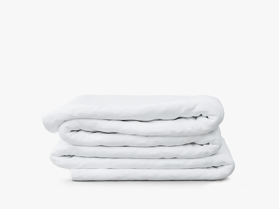 Stacked white bedding including sheets, duvet, and pillows