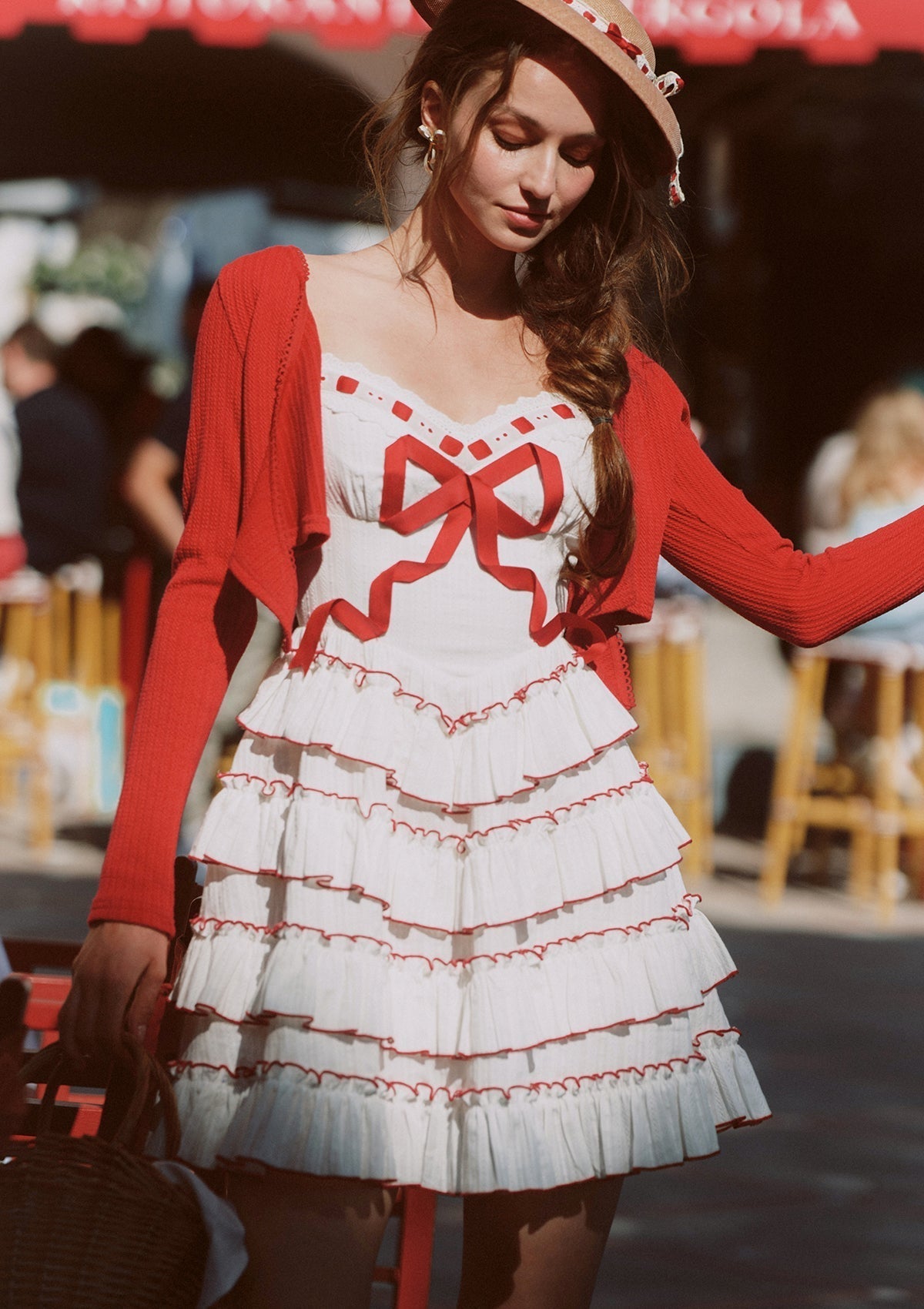 Close-up of a woman wearing a white tiered mini dress with red trim and bow detail, with a red cardigan