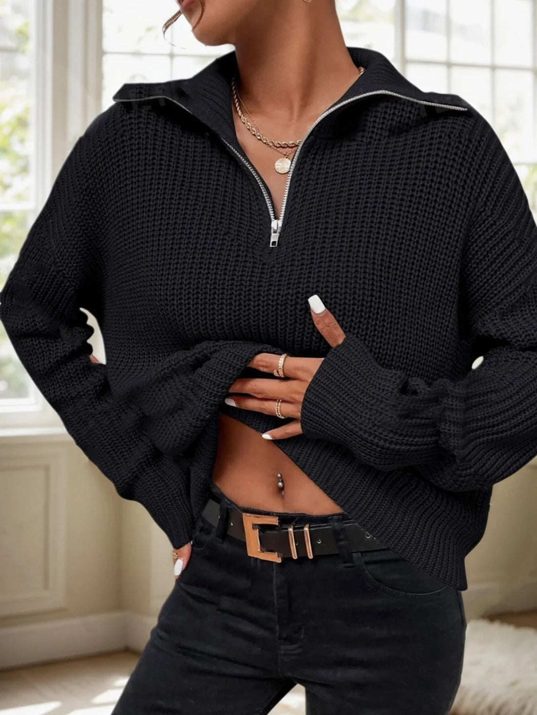 Woman wearing a black knit half-zip sweater with a pointed collar and silver zipper.