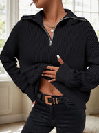 Woman wearing a black knit half-zip sweater with a pointed collar and silver zipper.