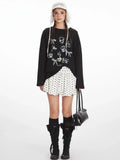 Woman wearing a black long-sleeved t-shirt with a graphic print, white polka dot skirt, black knee-high socks, and black boots.