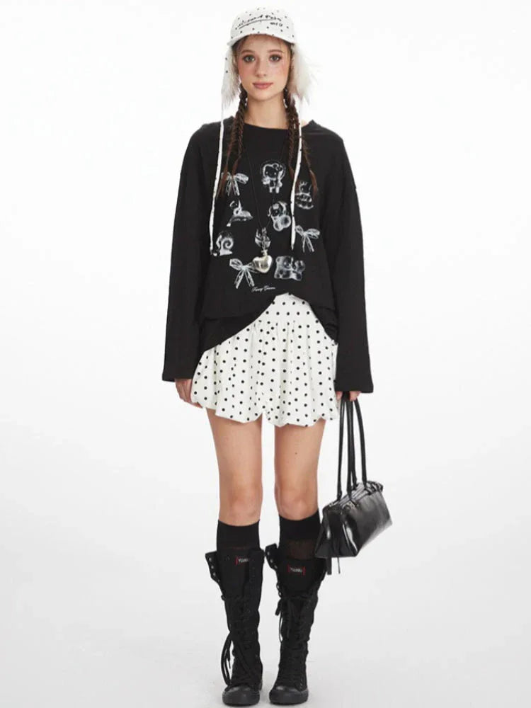 Woman wearing a black long-sleeved t-shirt with a graphic print, white polka dot skirt, black knee-high socks, and black boots.