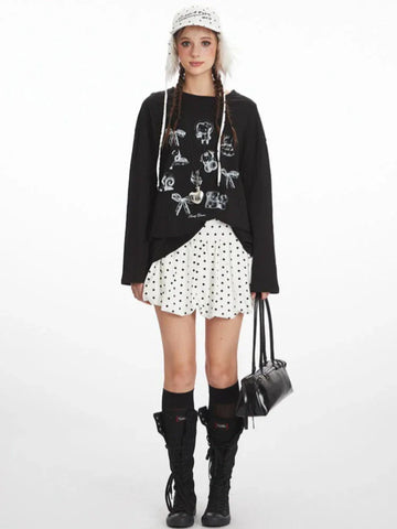 Woman wearing a black long-sleeved t-shirt with a graphic print, white polka dot skirt, black knee-high socks, and black boots.