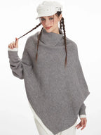 Close-up of a woman wearing a grey knit poncho with a turtleneck and batwing sleeves, showing the texture of the knit.