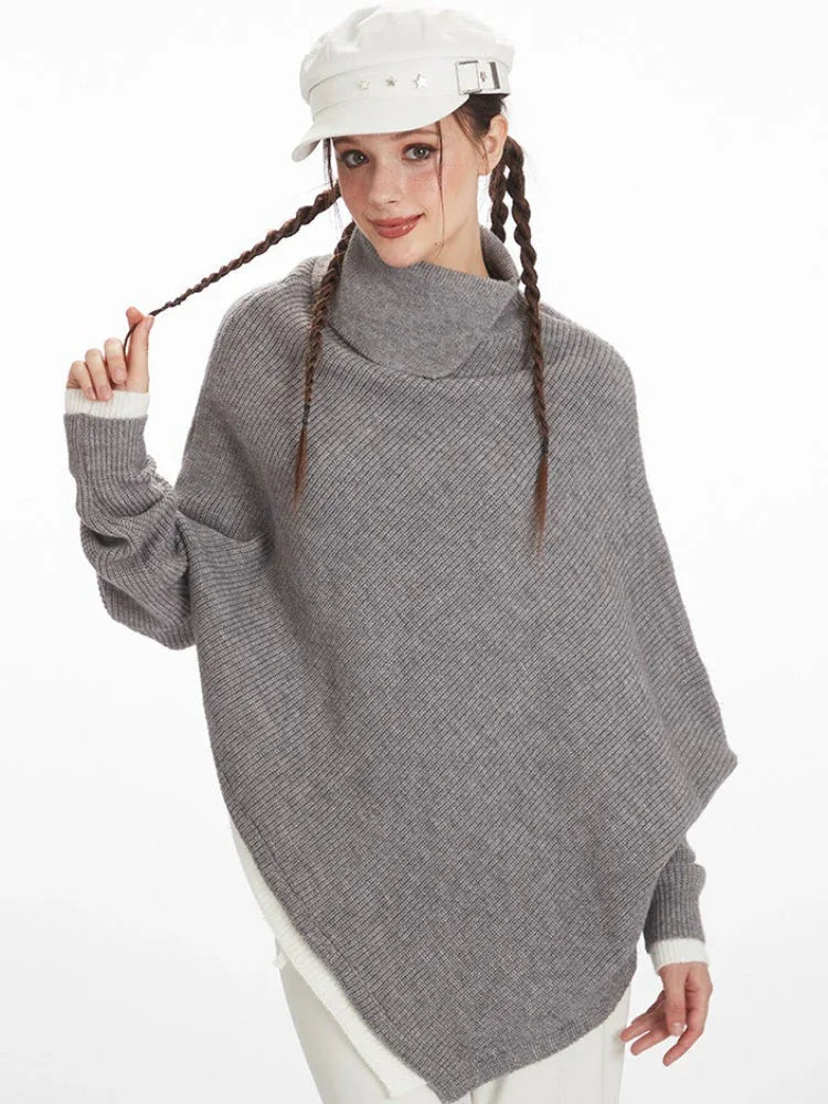 Close-up of a woman wearing a grey knit poncho with a turtleneck and batwing sleeves, showing the texture of the knit.