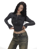 Woman wearing a dark grey long-sleeve graphic print cropped top and distressed wide-leg jeans.