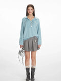 Model wearing a light blue fuzzy knit long-sleeve collared v-neck sweater with a ribbed hem, paired with a grey pleated mini skirt, grey boots, and a silver handbag.