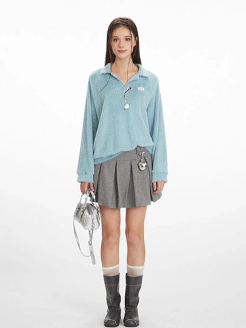 Model wearing a light blue fuzzy knit long-sleeve collared v-neck sweater with a ribbed hem, paired with a grey pleated mini skirt, grey boots, and a silver handbag.