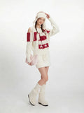 Model posing with a pink handbag and cream knit boots, wearing a cream sweater and skirt set.