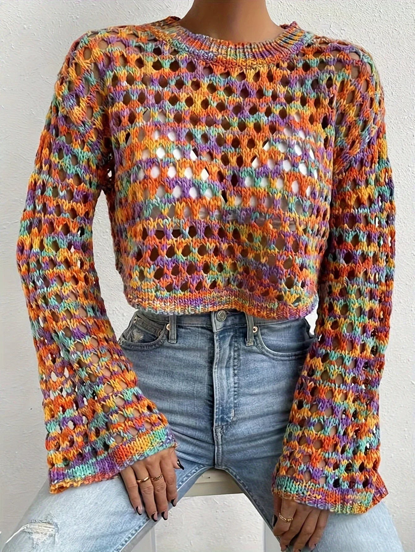 Full body shot of a woman in a multi-color cropped hollow-out knit sweater and light wash jeans
