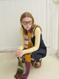 Woman in a yellow long-sleeve top, navy camisole, denim skirt, and a multi-colored striped fuzzy scarf, crouching.