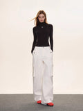 Full-body shot of a woman wearing a black turtleneck top and white wide-leg cargo pants.