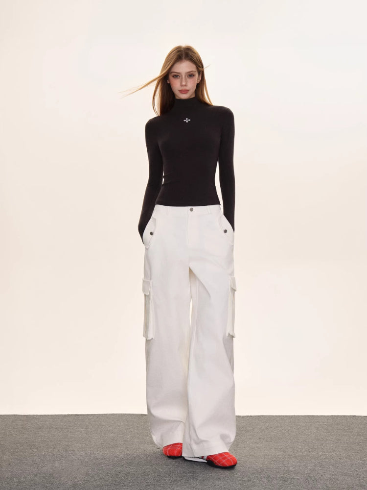 Full-body shot of a woman wearing a black turtleneck top and white wide-leg cargo pants.