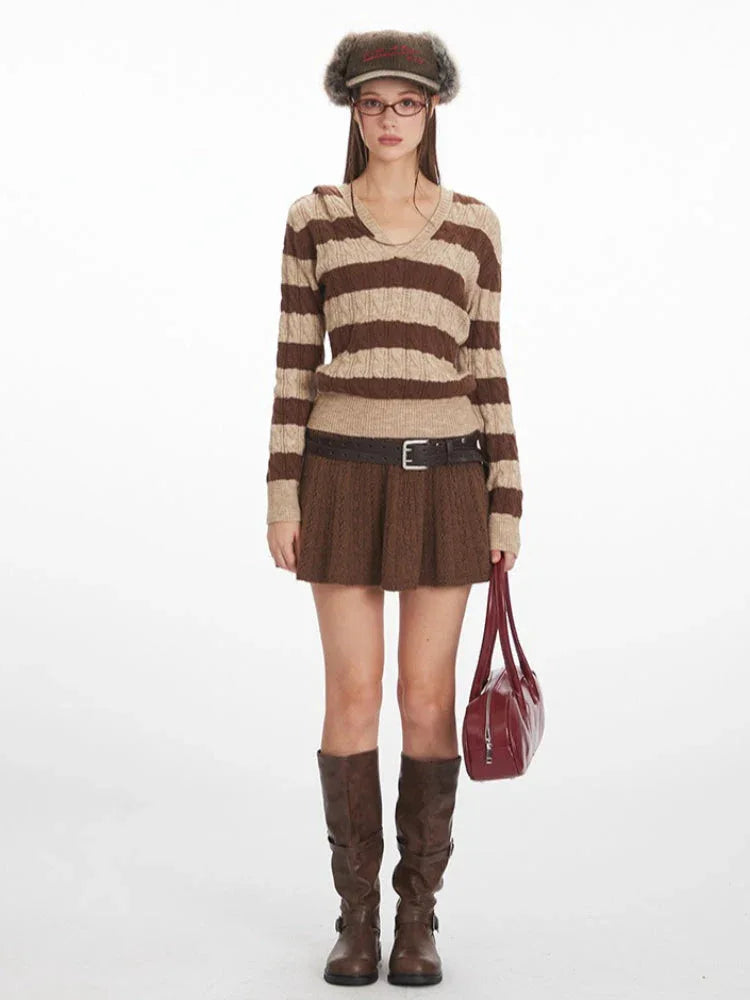 Woman wearing a brown and beige striped knit hooded sweater with a v-neckline and long sleeves, paired with a brown textured mini skirt and brown boots.
