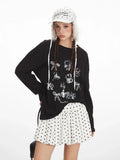 Close-up of a woman wearing a black long-sleeved t-shirt with a graphic print and white polka dot skirt.