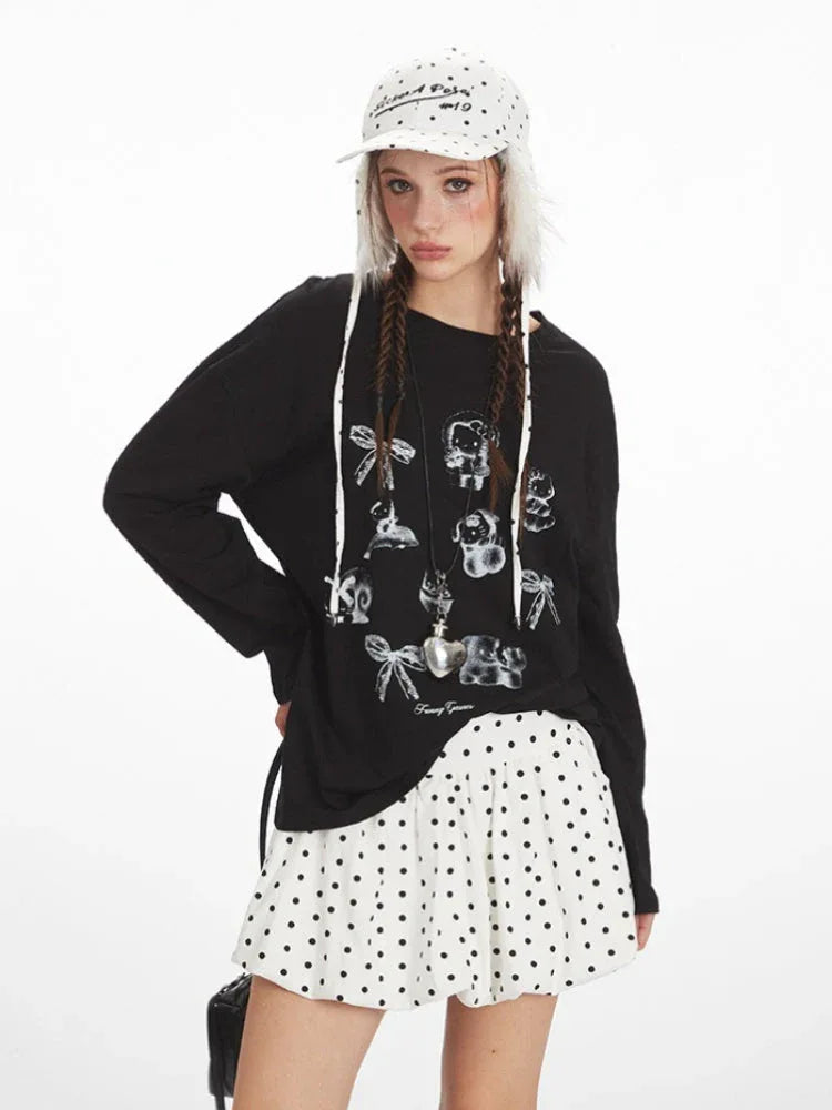 Close-up of a woman wearing a black long-sleeved t-shirt with a graphic print and white polka dot skirt.