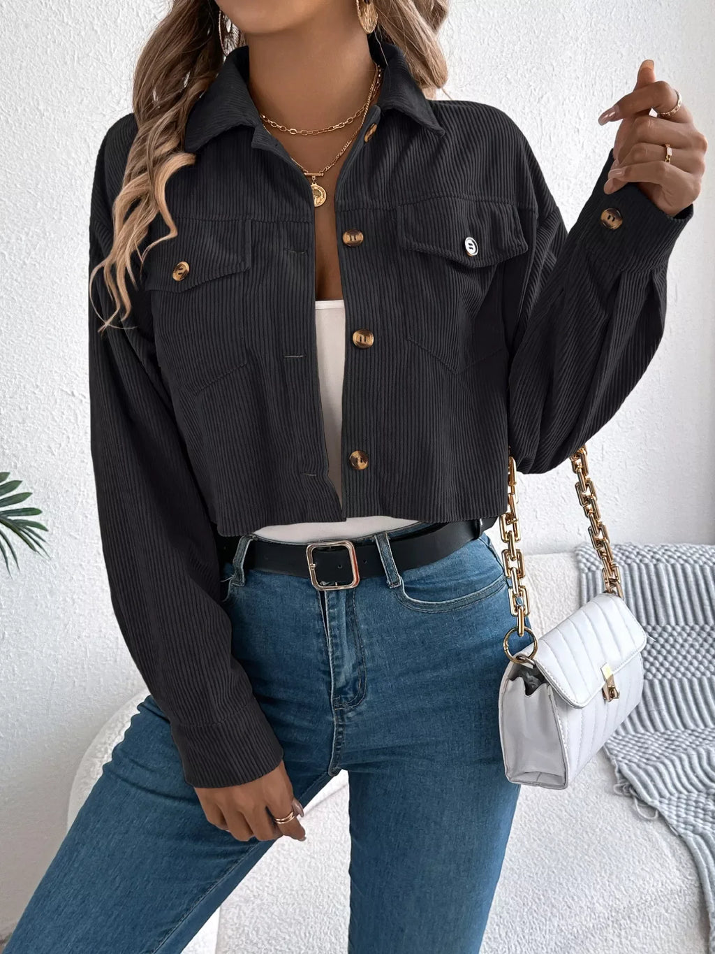 Woman with a white handbag, wearing a black cropped corduroy jacket and blue jeans