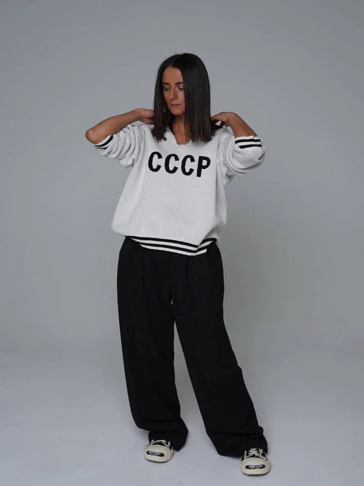 Woman wearing a white knit sweater with CCCP graphic print and black stripes on cuffs and hem.