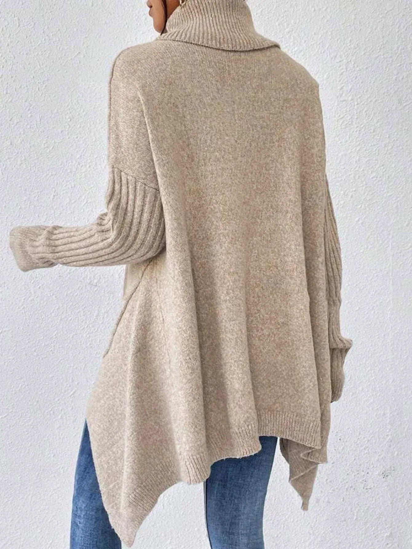 Back view of a woman in a beige knit turtleneck sweater with ribbed long sleeves and an asymmetrical hem.