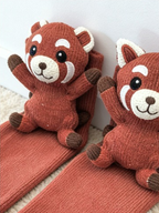 Close-up of two red knit crew socks, each featuring a red panda applique with embroidered facial features.