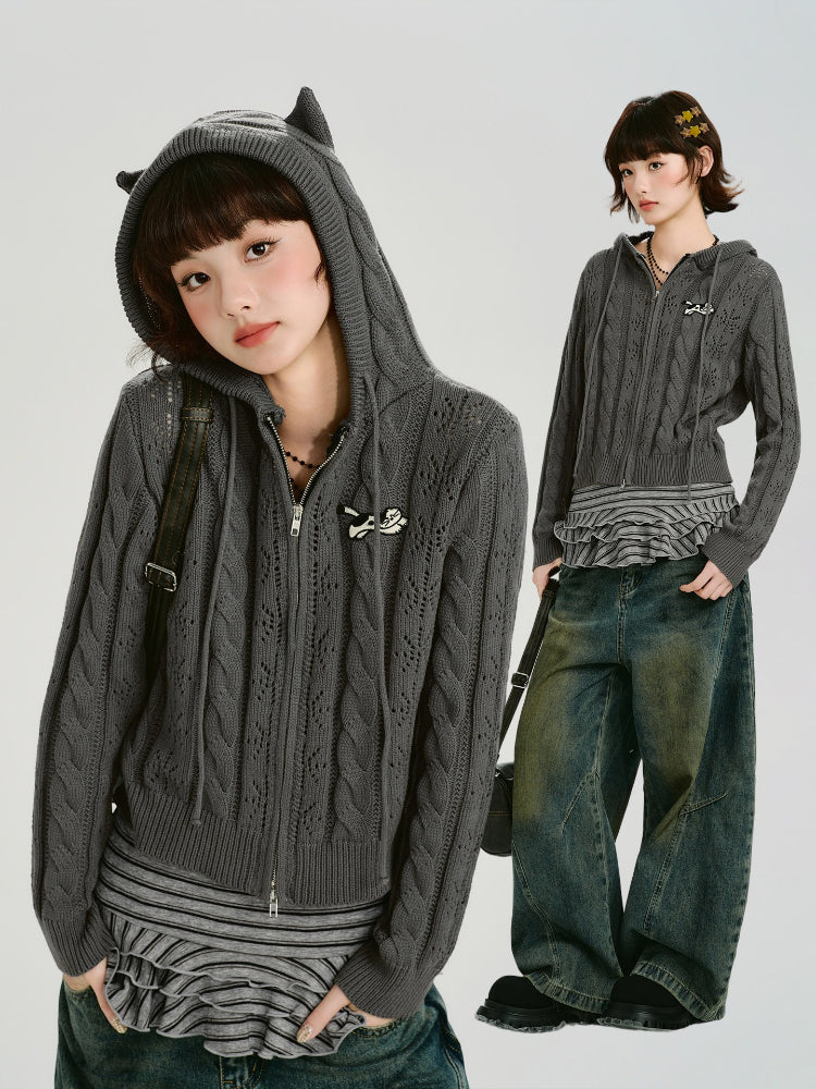 Model wearing a grey cable knit cropped hooded jacket with ear details, paired with striped top and jeans.