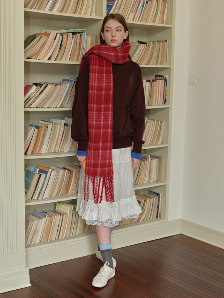 Woman wearing a white long-sleeved shirt, white pleated skirt, grey polka dot tights, silver boots, and a grey plaid scarf with fringe.