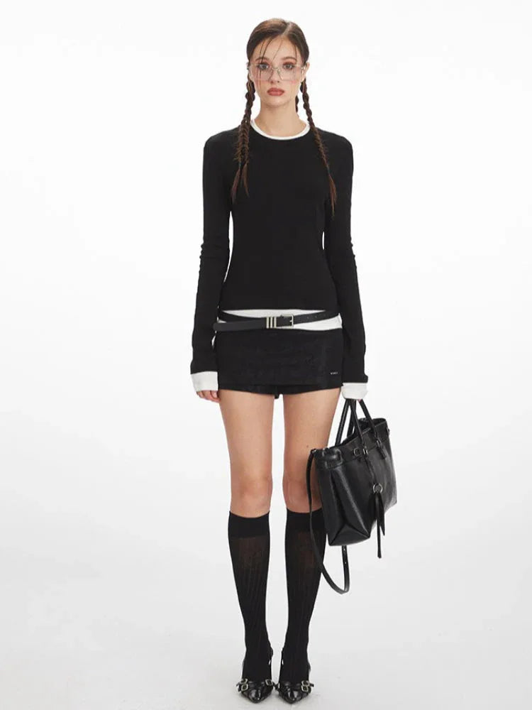 Model wearing a black long-sleeve top with white contrast trim at the neckline and cuffs, layered over a white band, paired with black shorts and knee-high socks.