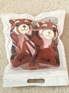 A pair of red knit crew socks with red panda appliques, packaged in a clear resealable plastic bag.