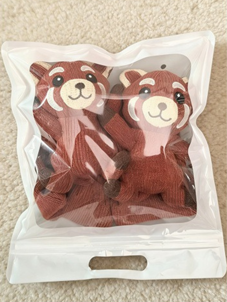 A pair of red knit crew socks with red panda appliques, packaged in a clear resealable plastic bag.