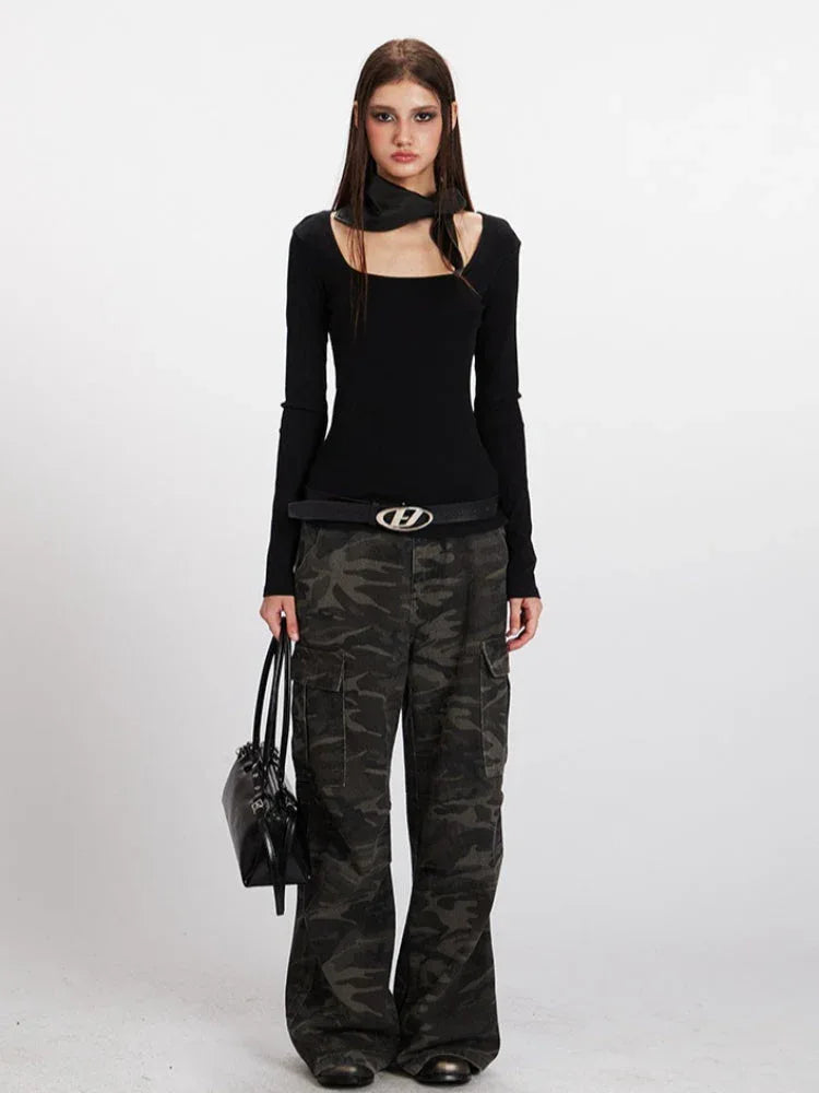 Model wearing a black long-sleeve ribbed top with a square neckline and a detachable scarf, paired with camouflage cargo pants and a black belt.