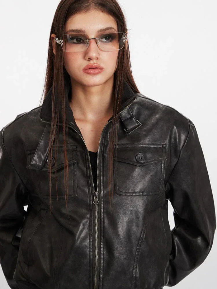 Detail of the chest pockets and zipper on a black faux leather bomber jacket.