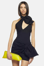 Model wearing a black asymmetrical mini dress with a halter neckline and bow detail