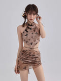 Woman wearing a brown sheer mesh two-piece set with a butterfly print, featuring a halter crop top and a mini skirt.