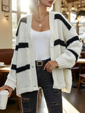 Woman wearing a white and black striped oversized knit cardigan with a white tank top and distressed black jeans.