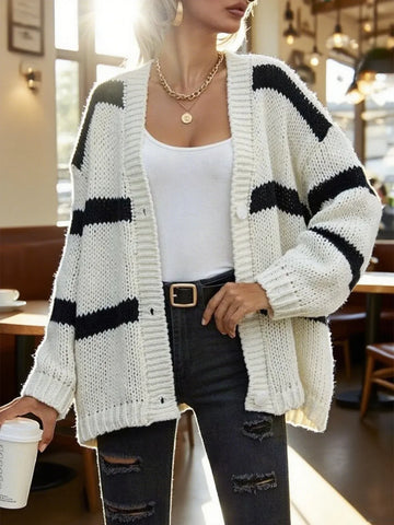 Woman wearing a white and black striped oversized knit cardigan with a white tank top and distressed black jeans.