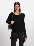 Woman holding a black handbag while wearing a black long-sleeve asymmetrical knit sweater