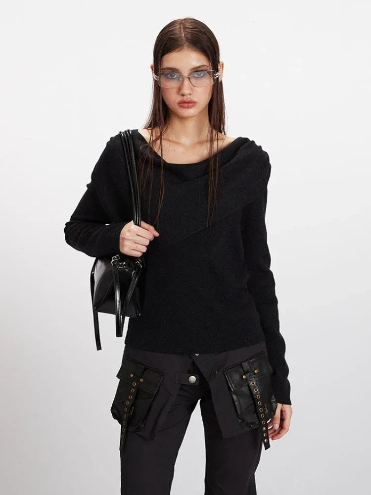 Woman holding a black handbag while wearing a black long-sleeve asymmetrical knit sweater