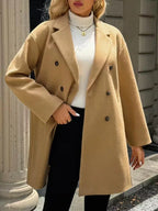 Full body shot of a woman in a camel double-breasted coat, standing outdoors.