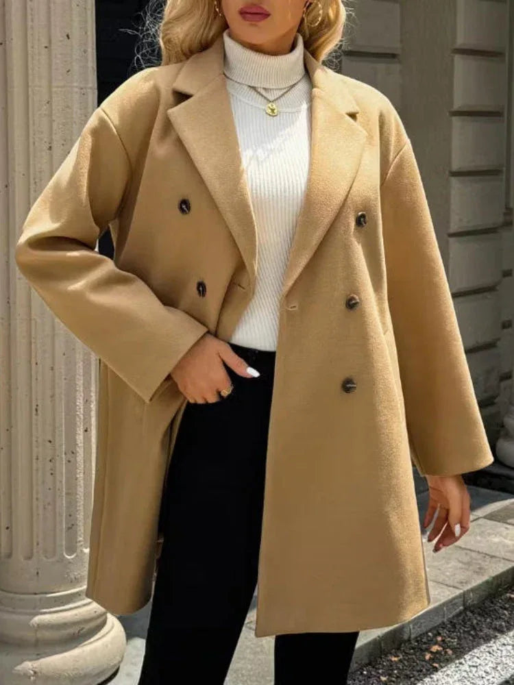 Full body shot of a woman in a camel double-breasted coat, standing outdoors.